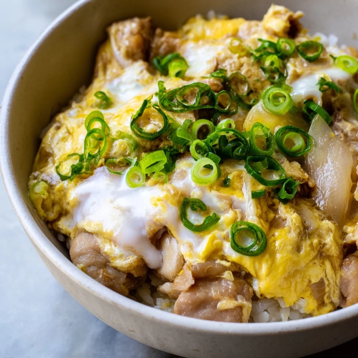 Homemade Oyakodon served in traditional donburi bowl with runny eggs and sliced green onions
