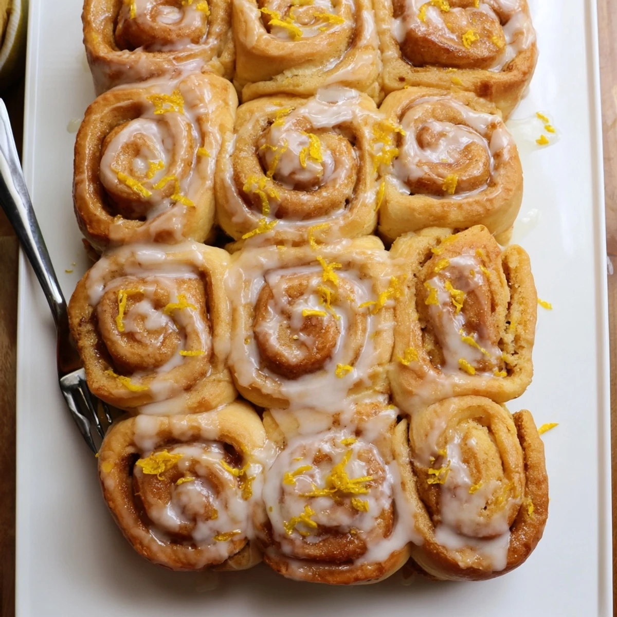 Freshly baked lemon rolls drizzled with tangy glaze on a white serving plate