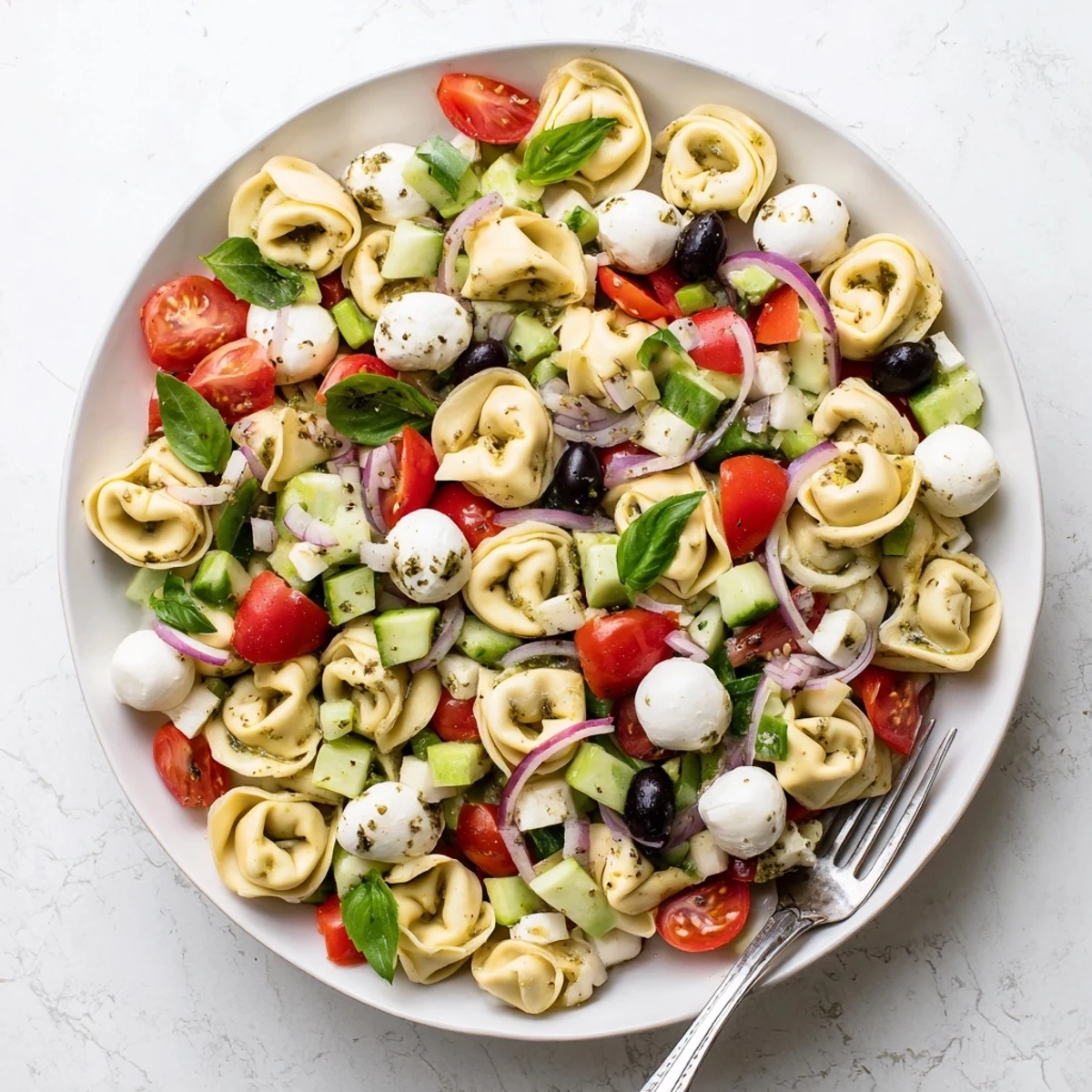 Colorful tortellini pasta salad in a bowl with cherry tomatoes, cucumber, and zesty Italian dressing