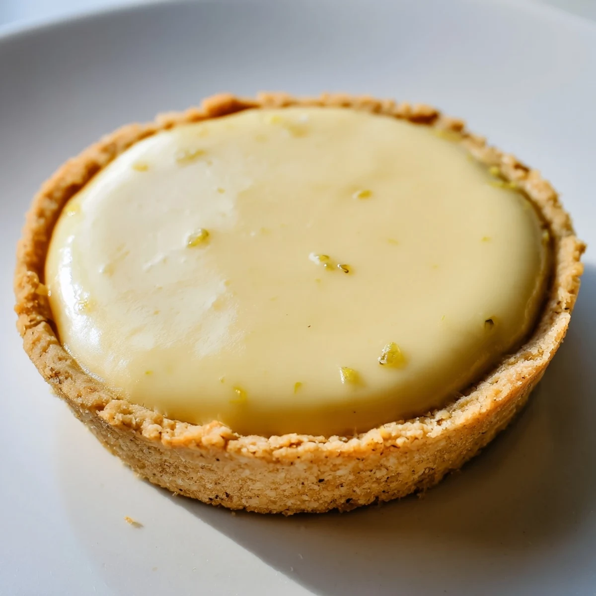 Creamy mini vegan lemon tarts in crisp almond crusts garnished with lemon zest