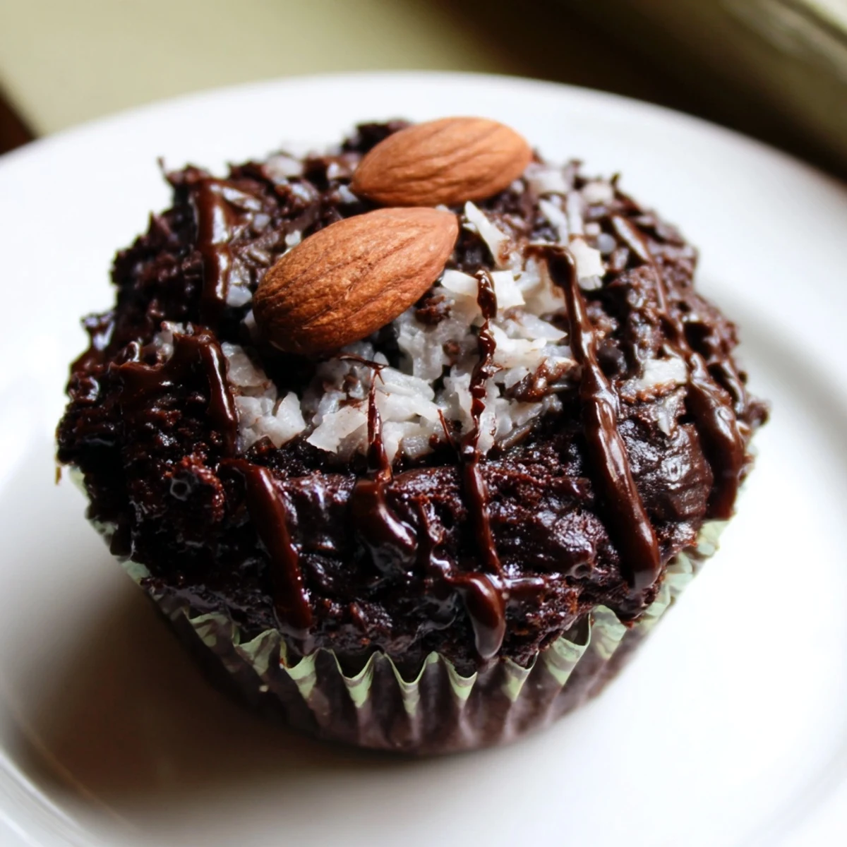 Rich flourless almond joy cupcakes topped with melted chocolate and roasted almonds on rustic parchment