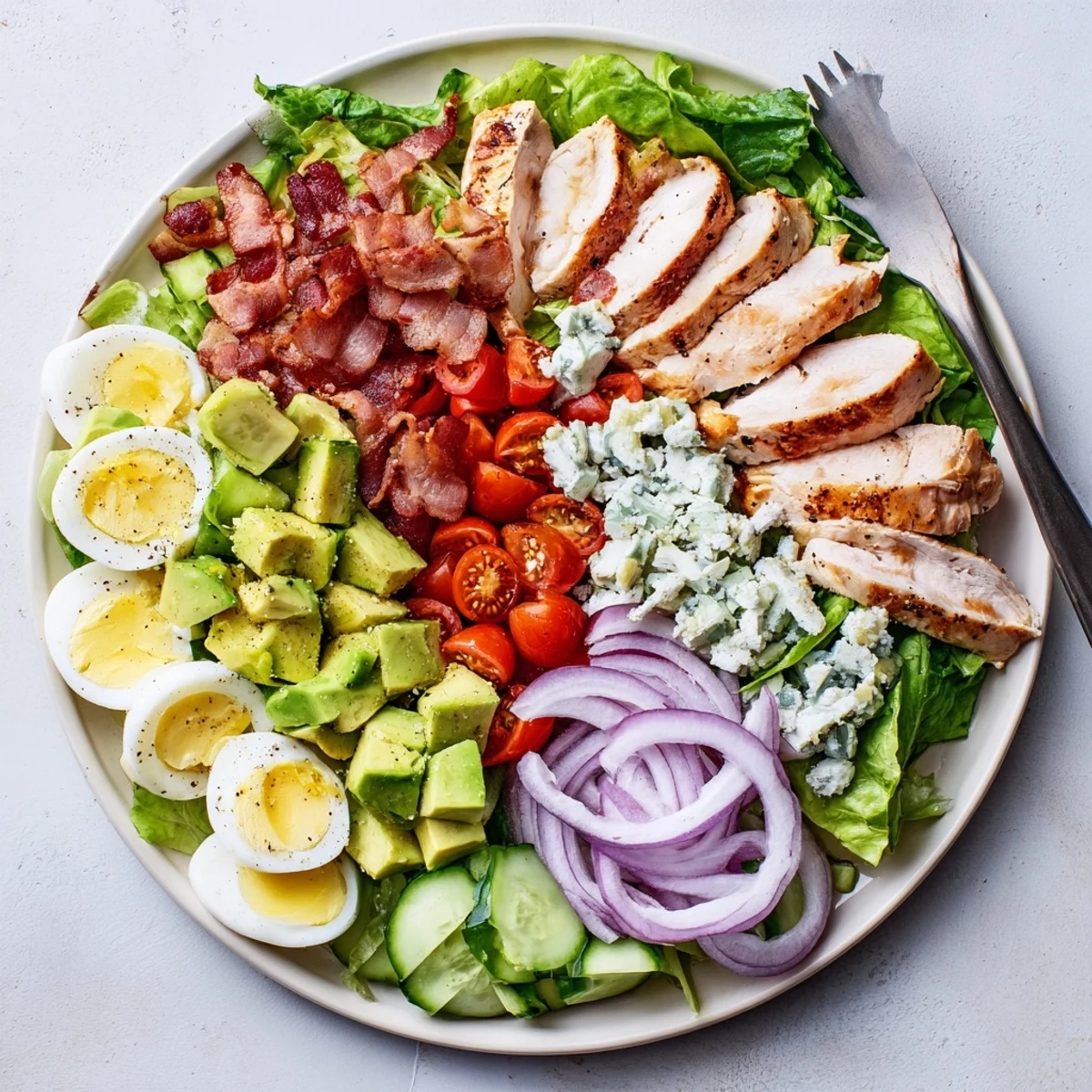 Colorful Paleo Grilled Chicken Cobb Salad topped with avocado, bacon, eggs, and fresh vegetables on a white platter