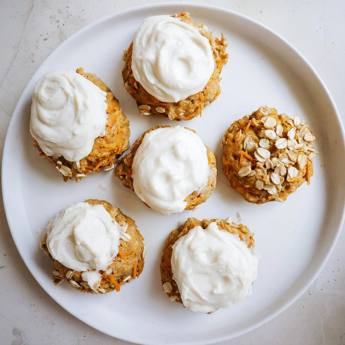 Bite-sized carrot cake cookies drizzled with sweet cream cheese frosting on a white plate