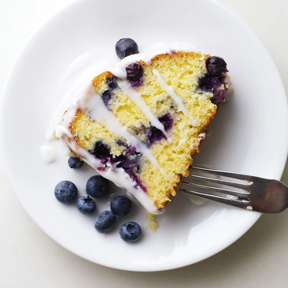 Golden lemon blueberry cake drizzled with white glaze and fresh berry garnish on serving plate