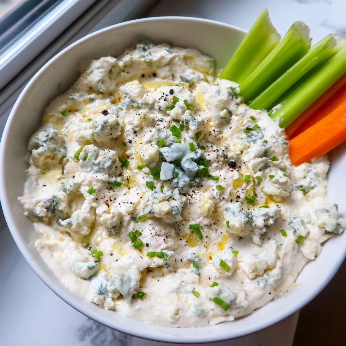 Thick, velvety blue cheese dip garnished with crumbled cheese and minced chives, perfect for game-day snacking.