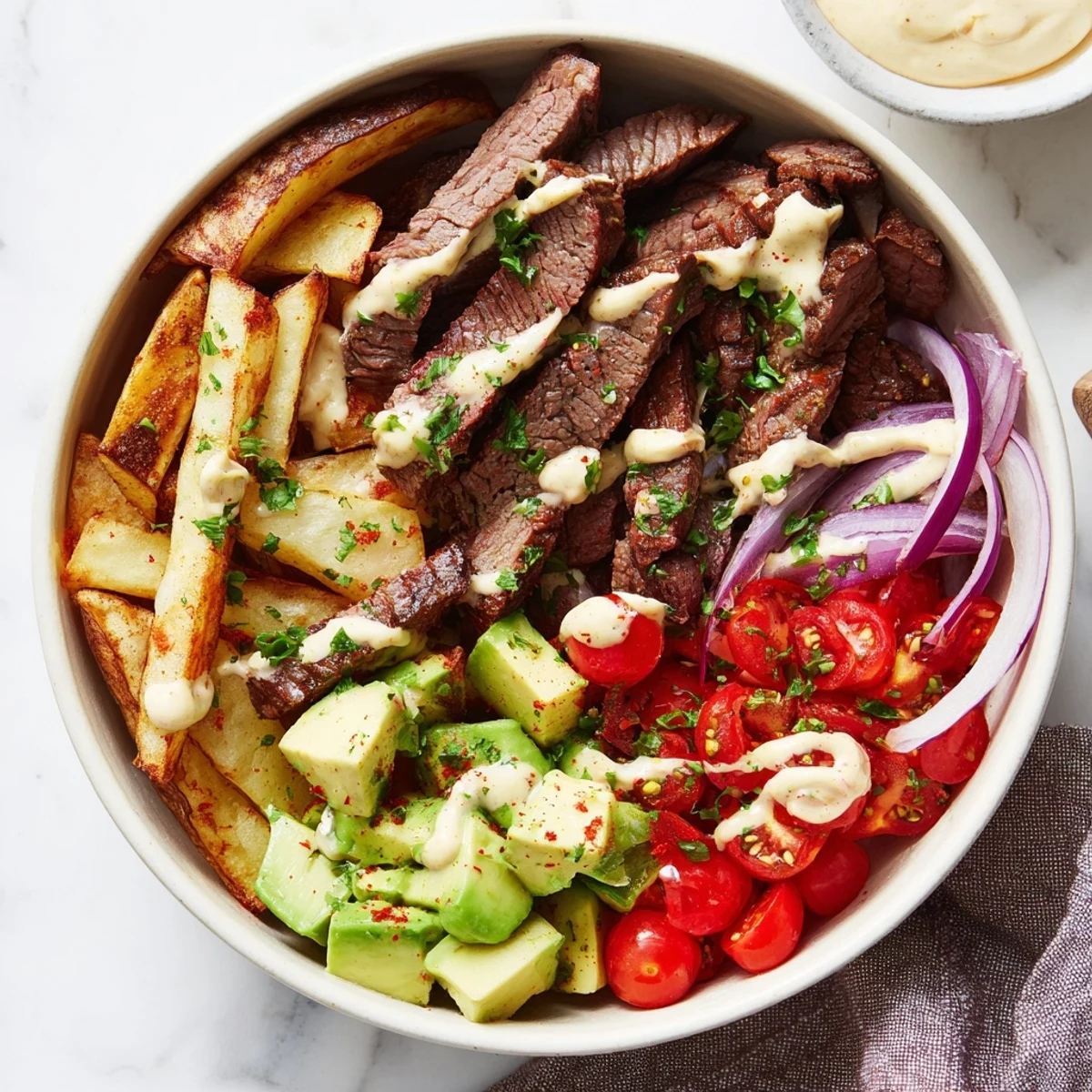 Juicy steak strips and crispy fries bowl drizzled with creamy mustard sauce